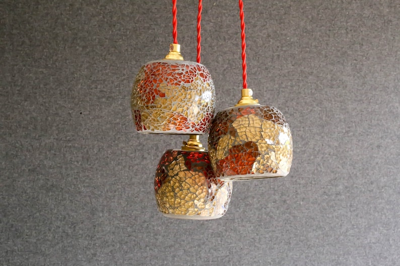 May include: Three glass pendant lights with red and gold mosaic tile designs hanging from red cords.