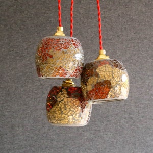 May include: Three hanging light fixtures with red cords. The light fixtures are made of glass mosaic tiles in shades of gold, brown, and red.
