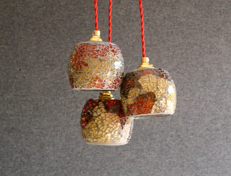 May include: Three hanging light fixtures with red cords. The light fixtures are made of glass mosaic tiles in shades of gold, brown, and red.