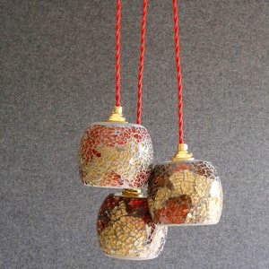May include: Three hanging pendant lights with red cords. The lights are made of glass with a mosaic pattern in shades of gold, brown, and red.