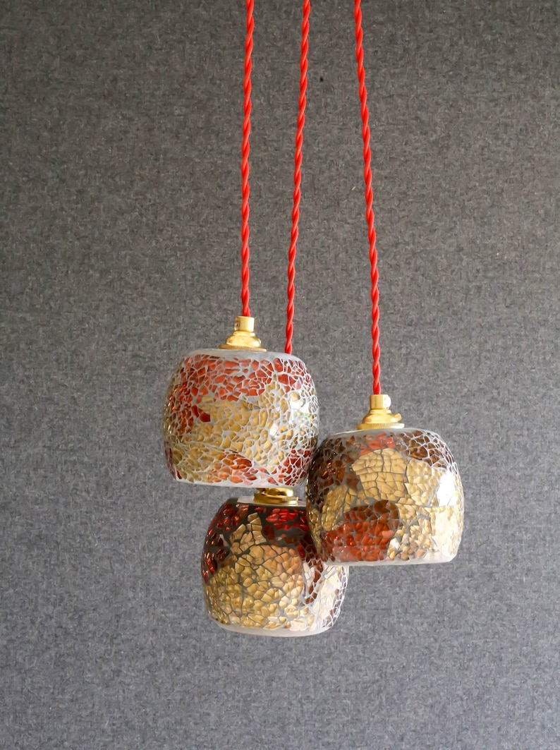 May include: Three hanging pendant lights with red cords. The lights are made of glass with a mosaic pattern in shades of gold, brown, and red.