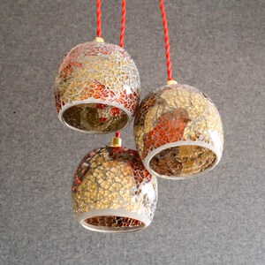 May include: Three hanging pendant lights with red cords. The lights are made of glass with a mosaic pattern of gold and red.