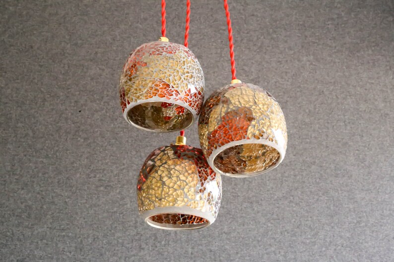 May include: Three hanging pendant lights with red cords. The lights are made of glass with a mosaic pattern of gold and red.