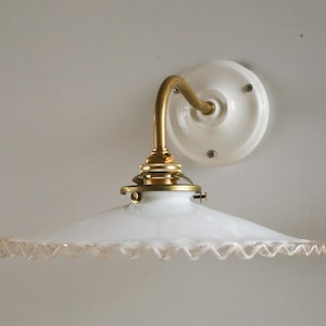 May include: A white porcelain wall sconce with a brass arm and a white glass shade with a scalloped edge.