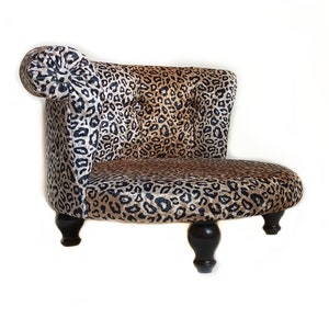 May include: A small, leopard-print chair with a rounded back and armrest. The chair has a tufted back and a curved seat. The legs are dark brown and rounded. The chair is designed for a pet.