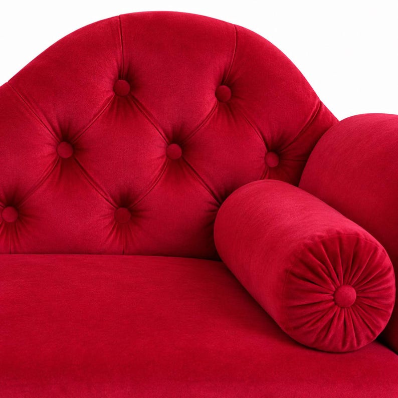 May include: A bright red velvet chaise longue featuring a curved backrest with deep button tufting. The furniture piece includes a matching cylindrical bolster pillow positioned on the seat, showcasing a soft, plush texture throughout the design.