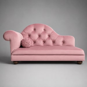 May include: A pink velvet chaise longue featuring a tufted backrest with button detailing, a curved armrest, and a matching round bolster cushion. The furniture piece is supported by four dark brown wooden feet and has a smooth, upholstered seat.