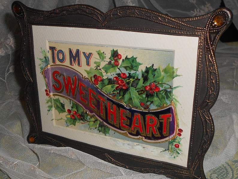 May include: A framed vintage holiday card with a gold, purple, and red banner that reads "To My Sweetheart". The banner is surrounded by holly leaves and red berries.