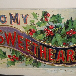 May include: A vintage Christmas card with a holly and berry design. The card features a banner with the text "To My Sweetheart" in red and gold lettering.