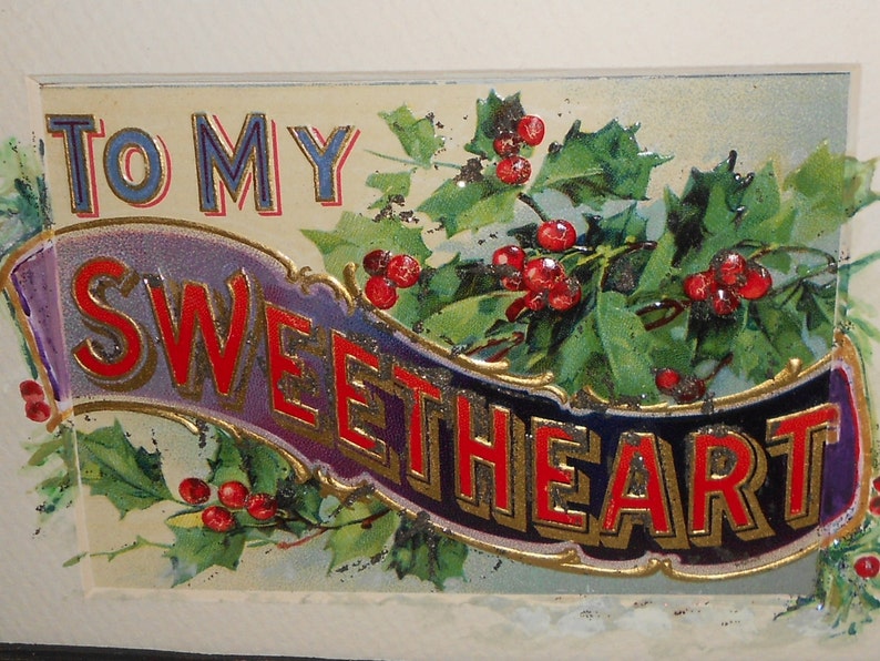 May include: A vintage Christmas card with a holly and berry design. The card features a banner with the text "To My Sweetheart" in red and gold lettering.