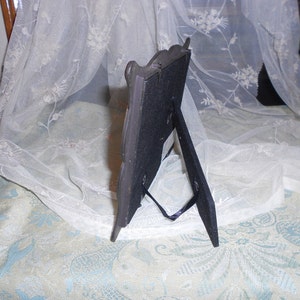 May include: A black picture frame with a decorative silver design. The frame has a stand on the back and is made of metal.