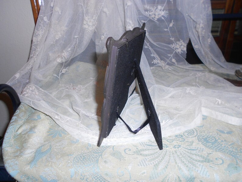May include: A black picture frame with a decorative silver design. The frame has a stand on the back and is made of metal.