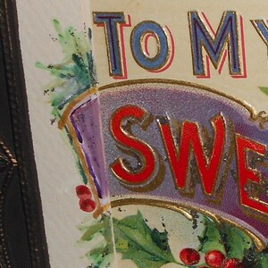 May include: A vintage greeting card with a purple, gold, and red banner that reads "To My Sweetheart". The banner is decorated with green holly leaves and red berries.