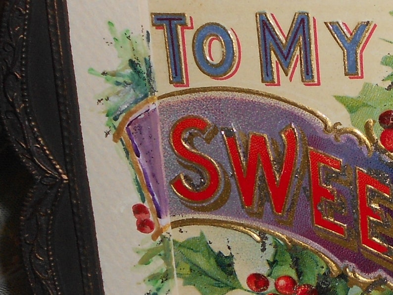 May include: A vintage greeting card with a purple, gold, and red banner that reads "To My Sweetheart". The banner is decorated with green holly leaves and red berries.