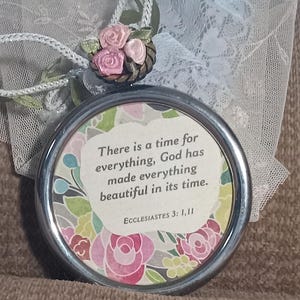 May include: A silver-toned round ornament with a floral design and the quote "There is a time for everything, God has made everything beautiful in its time. Ecclesiastes 3: 1,11"