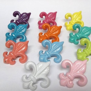 May include: Assortment of 12 colorful fleur-de-lis shaped metal drawer pulls in various colors including pink, blue, green, orange, yellow, and purple.
