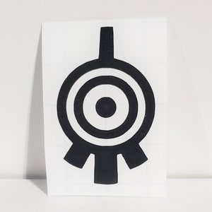 May include: Black sticker featuring a stylized, symmetrical design. The design consists of a central circle surrounded by concentric rings, with a vertical bar extending upwards and three downward-pointing shapes at the base. The sticker is on a white background.