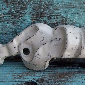 May include: White metal drawer pull with a distressed finish and a wavy, organic design. The pull has two holes for mounting.