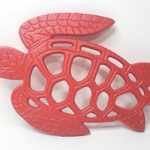May include: Red cast iron turtle shaped hot pad. The turtle has a detailed shell design with cutouts.