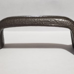 May include: A dark gray metal door handle with a textured finish. The handle has a curved shape and two sets of screw holes on each side.