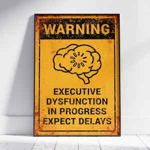 May include: A framed sign with a distressed yellow background and black text. The top of the sign reads "WARNING" above a black brain illustration. Below the brain, the sign reads "EXECUTIVE DYSFUNCTION IN PROGRESS EXPECT DELAYS."