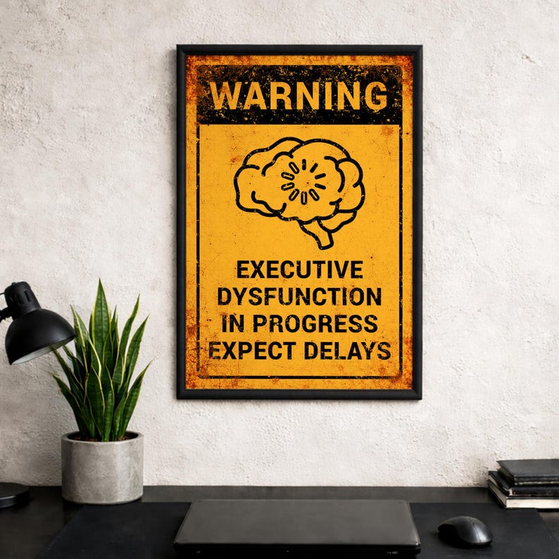 May include: A framed poster with a yellow background and black text that reads "WARNING EXECUTIVE DYSFUNCTION IN PROGRESS EXPECT DELAYS." The poster features a brain graphic and a distressed, vintage style.