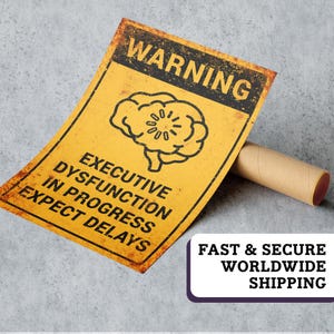 May include: A yellow metal sign with the text "WARNING" at the top and "EXECUTIVE DYSFUNCTION IN PROGRESS EXPECT DELAYS" below a brain graphic. The sign has a distressed, aged appearance. A brown cardboard tube rests beside the sign.