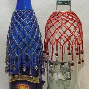 Puede incluir: Dos botellas de vino decoradas. Una es azul con una red de cuentas y cuentas colgantes. La otra es transparente con una red de cuentas rojas. La botella azul tiene la palabra "Riesling". La otra botella tiene las palabras "Prairie Fume".
