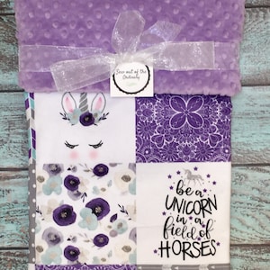 May include: Purple and white baby blanket with a unicorn, flowers, and the text "be a unicorn in a field of horses".