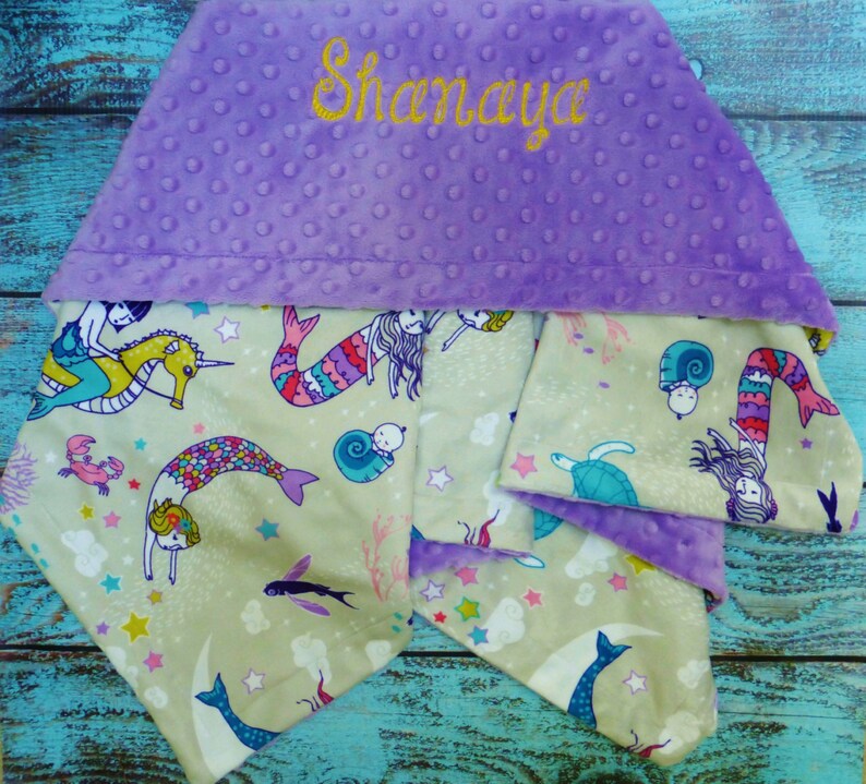 May include: A purple hooded baby blanket with a mermaid and seahorse design. The blanket is personalised with the name "Shanaya".