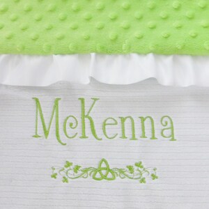 May include: White baby blanket with green embroidery of the name McKenna and a Celtic knot with shamrocks.