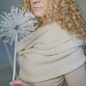 Könnte beinhalten: Eine Frau mit langen, lockigen blonden Haaren trägt einen weißen Strick Schal. Der Schal ist um ihren Hals und ihre Schultern gelegt. Sie hält eine weiße, dekorative Blume.