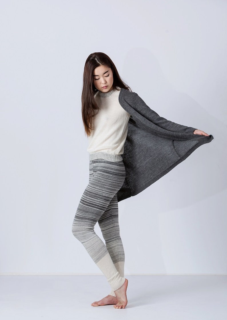 Puede incluir: Una mujer con un su&eacute;ter blanco, leggings a rayas grises y blancas y un c&aacute;rdigan gris. Est&aacute; de pie con los brazos cruzados y mirando hacia abajo.