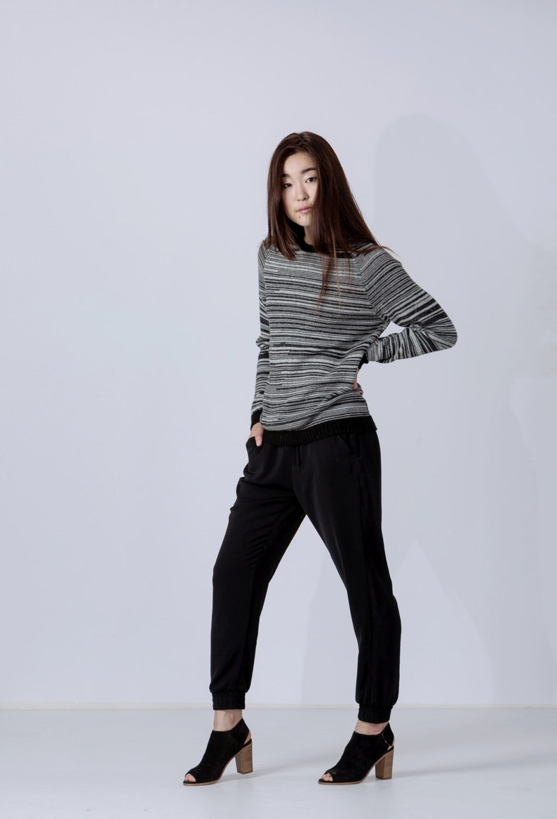 May include: A woman wearing a black and white striped sweater with black pants and black heeled shoes.