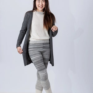 Puede incluir: Una mujer con un c&aacute;rdigan gris, un su&eacute;ter blanco y leggings a rayas grises y blancas con polainas de punto blancas.
