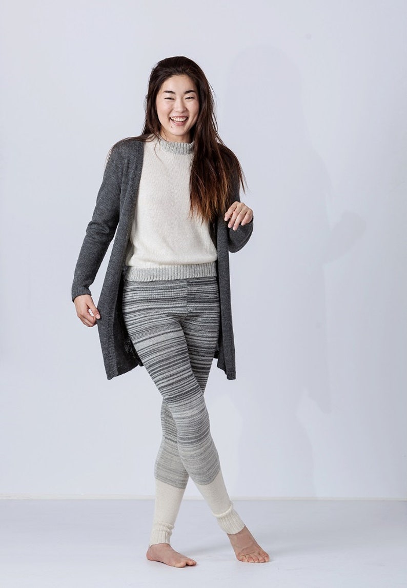 Puede incluir: Una mujer con un c&aacute;rdigan gris, un su&eacute;ter blanco y leggings a rayas grises y blancas con polainas de punto blancas.
