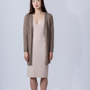 Puede incluir: Una mujer lleva una chaqueta de punto marr&oacute;n claro sobre un vestido de slip beige claro. Lleva zapatos de cuero marr&oacute;n claro con cordones.