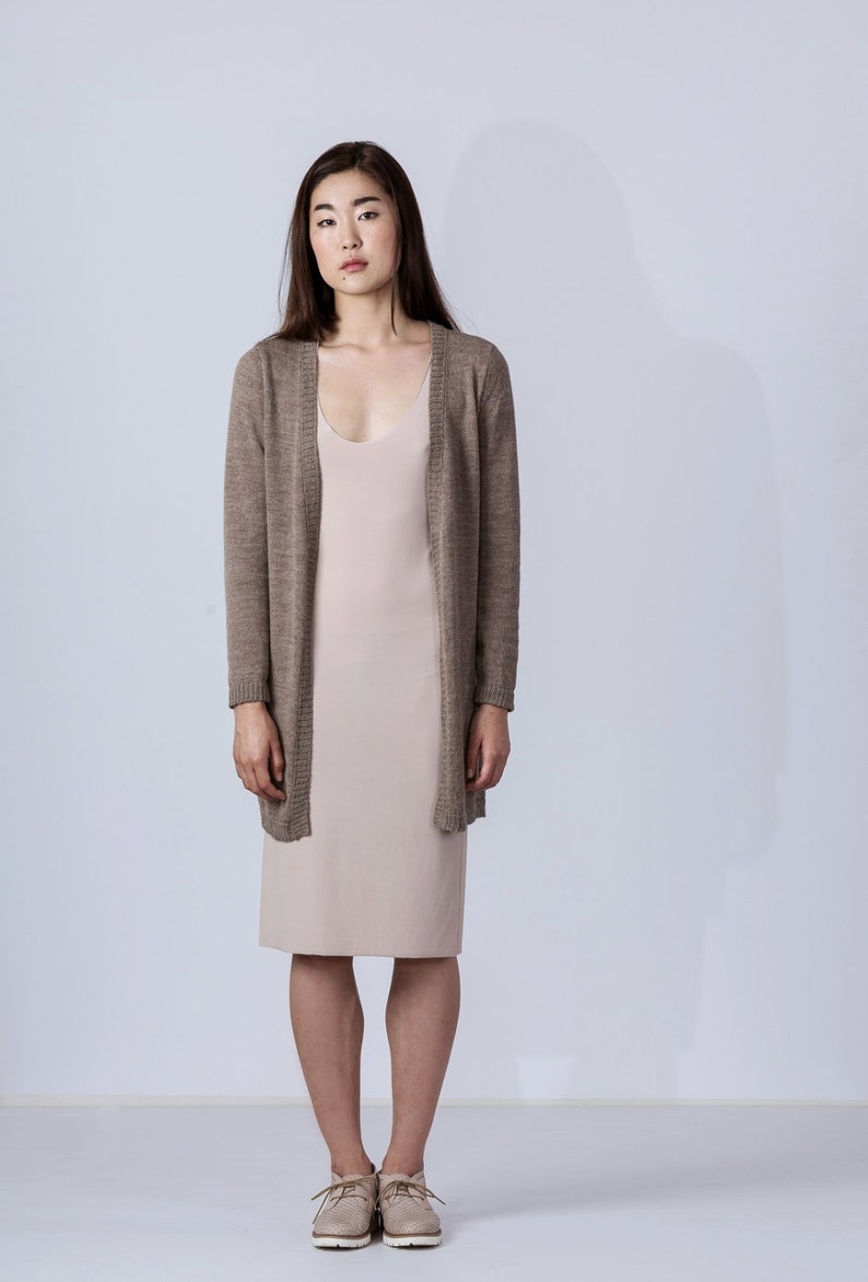 Puede incluir: Una mujer lleva una chaqueta de punto marr&oacute;n claro sobre un vestido de slip beige claro. Lleva zapatos de cuero marr&oacute;n claro con cordones.