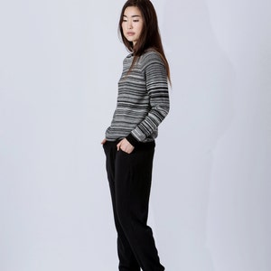 May include: A woman wearing a black and white striped sweater with black pants and black heeled shoes.