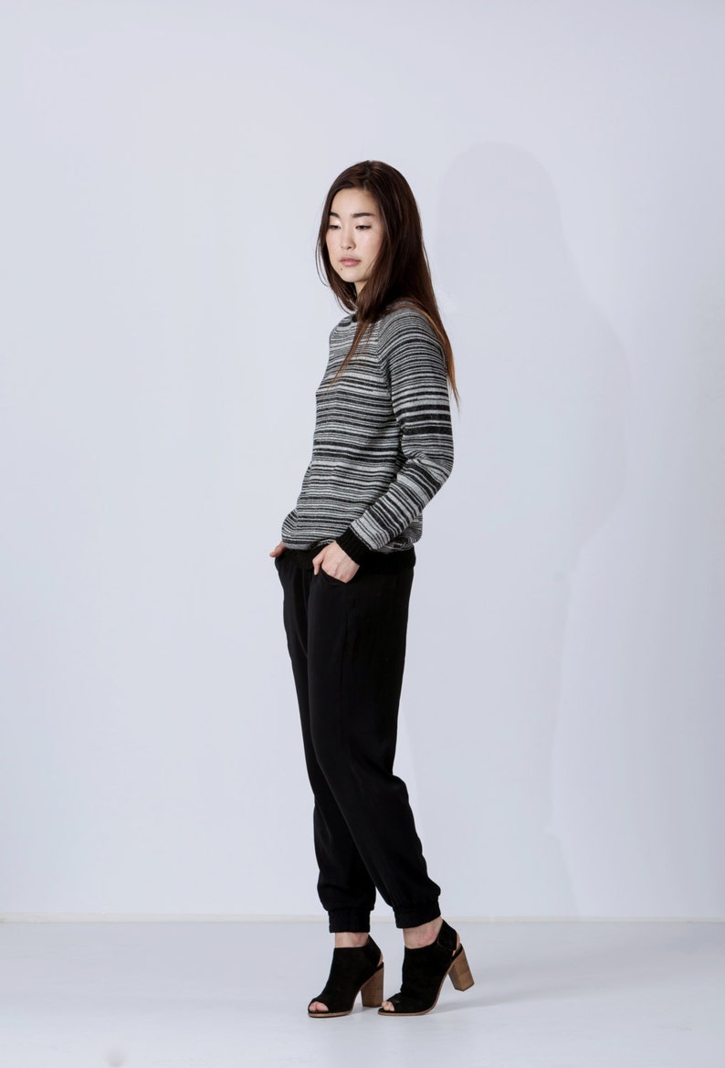 May include: A woman wearing a black and white striped sweater with black pants and black heeled shoes.
