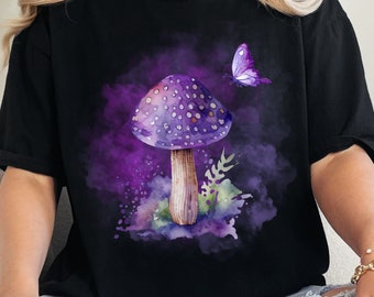 May include: A black t-shirt with a purple watercolor mushroom and butterfly design. The mushroom has white spots and is surrounded by green leaves.