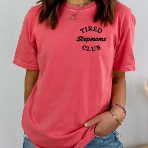 May include: A pink t-shirt with the text "TIRED Stepmoms CLUB" printed on the front.