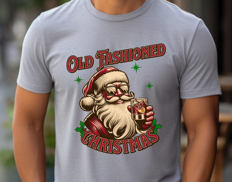 K&ouml;nnte beinhalten: Hellgraues T-Shirt mit einer Grafik von Santa Claus mit Sonnenbrille und einem Cocktail. Der Text "Old Fashioned Christmas" ist in Rot und Wei&szlig;, mit gr&uuml;nen Sternakzenten. Das Design ist festlich und weihnachtlich.