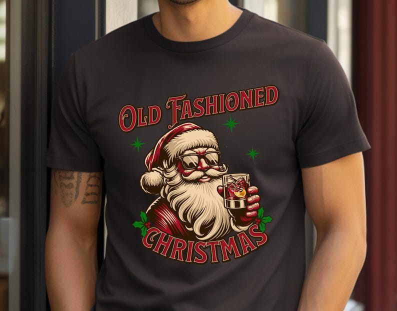 K&ouml;nnte beinhalten: Schwarzes T-Shirt mit einer Illustration von Santa Claus, der eine Sonnenbrille tr&auml;gt und einen Cocktail h&auml;lt. Der Text "Old Fashioned Christmas" ist oberhalb und unterhalb der Santa-Grafik angeordnet. Gr&uuml;ne Sternakzente sind enthalten.