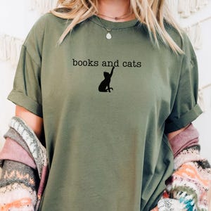 May include: A green t-shirt with the text "books and cats" and a silhouette of a cat reaching up printed on the front.