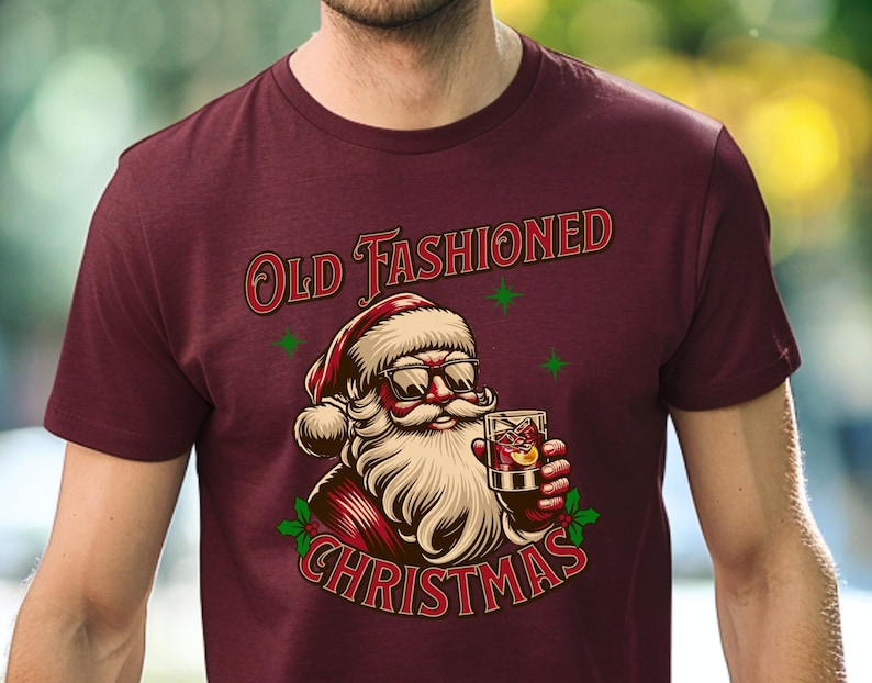 K&ouml;nnte beinhalten: Burgunderfarbenes T-Shirt mit einer Grafik von Santa Claus mit Sonnenbrille und einem Cocktail. Der Text "Old Fashioned Christmas" ist in Rot und Gr&uuml;n &uuml;ber und unter der Santa-Illustration angeordnet.