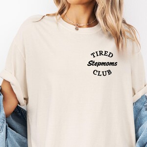 May include: A white t-shirt with the text "TIRED Stepmoms CLUB" in black lettering.
