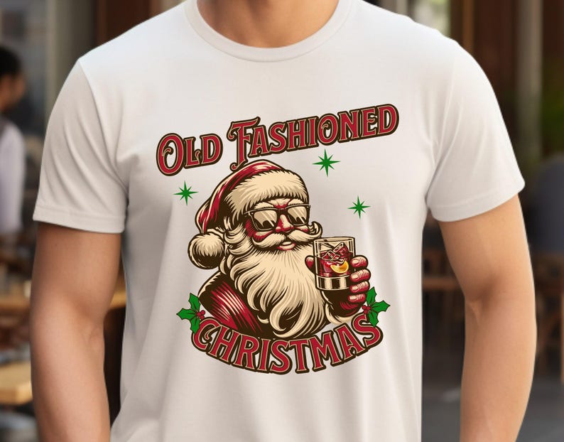 K&ouml;nnte beinhalten: Wei&szlig;es T-Shirt mit einem Cartoon-Weihnachtsmann, der eine Sonnenbrille tr&auml;gt und einen Cocktail h&auml;lt. Der Aufdruck "Old Fashioned Christmas" ist rot und gr&uuml;n, mit gr&uuml;nen Sternen.