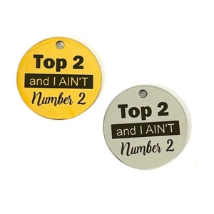 May include: Two round metal tags with the text "Top 2 and I AIN'T Number 2" in black lettering. One tag is gold and the other is silver.