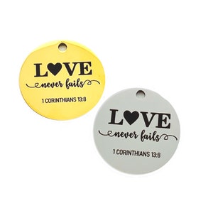 May include: Two round metal tags with the words "LOVE never fails" and the Bible verse "1 Corinthians 13:8". One tag is gold and the other is silver.
